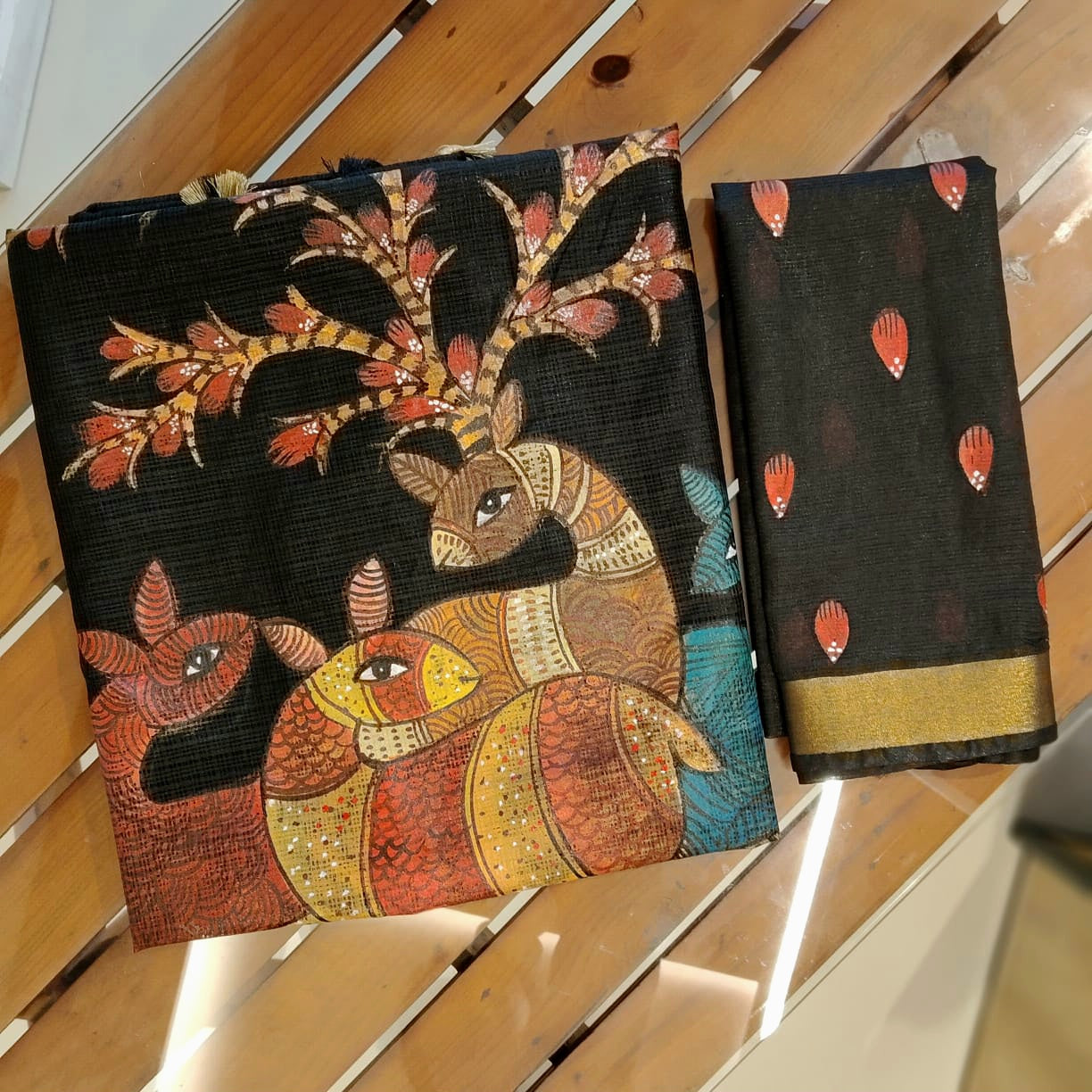 Two black sarees with intricate designs on a wooden surface